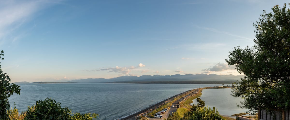 A coastal landscape with a long beach, a road parallel to the shore, and mountains in the distance.