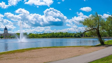 Un lago con una fuente, un parque con bancos, árboles y un edificio con cúpula al fondo.