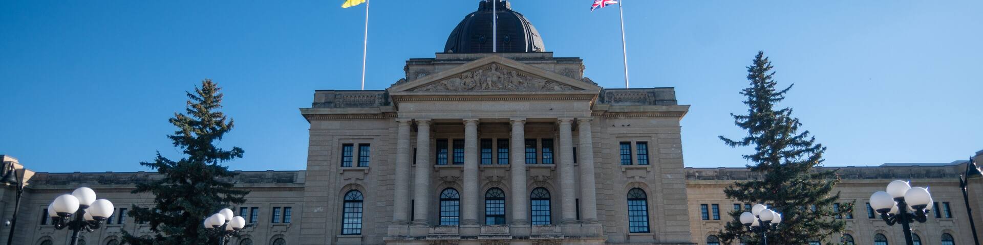 A large government building with a central dome, two flags, and a symmetrical facade.
