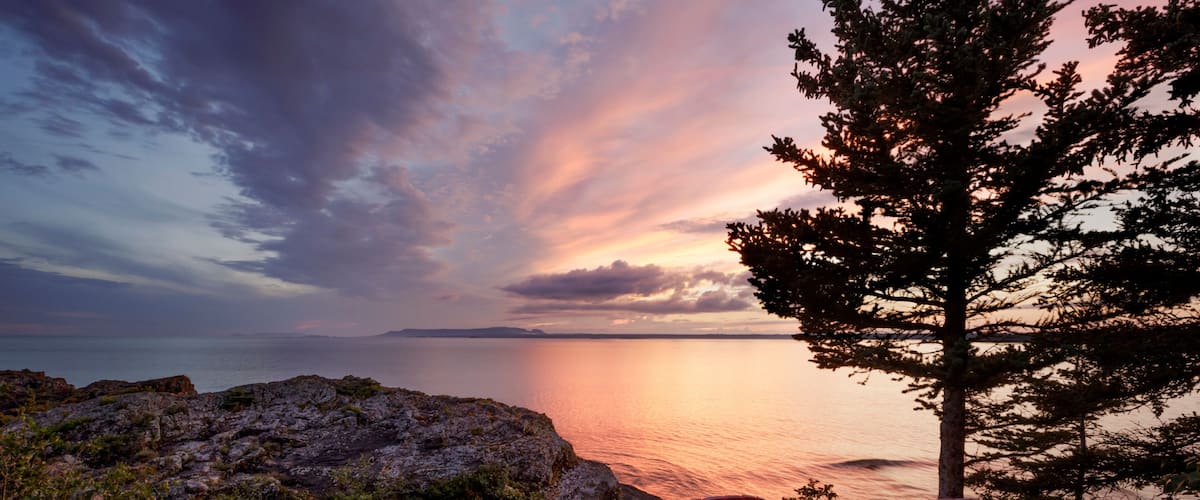Two red adirondack chairs on a rocky ridge with a view of the Sleeping Giant from Porphryry Island; Porphryry Island, Ontario, Canada