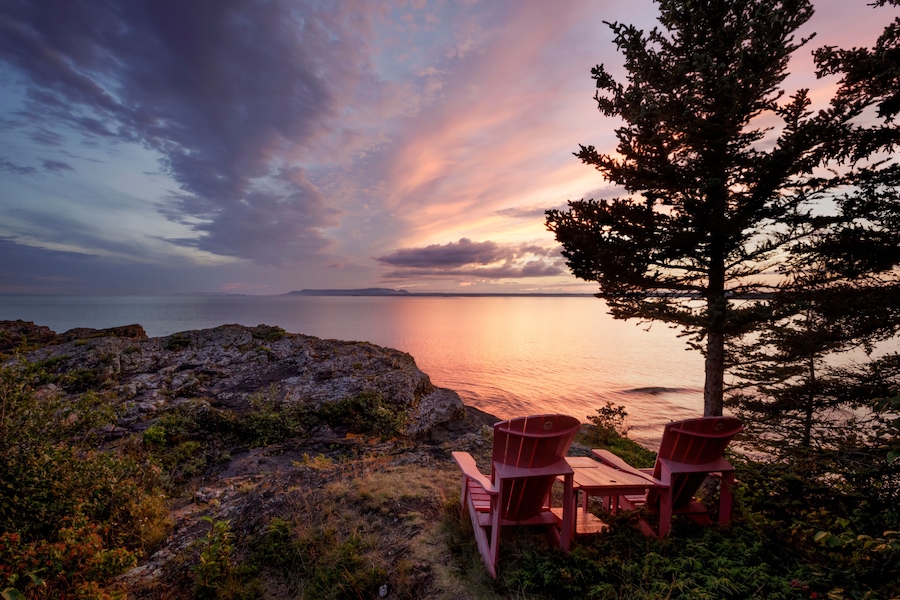 Two red adirondack chairs on a rocky ridge with a view of the Sleeping Giant from Porphryry Island; Porphryry Island, Ontario, Canada