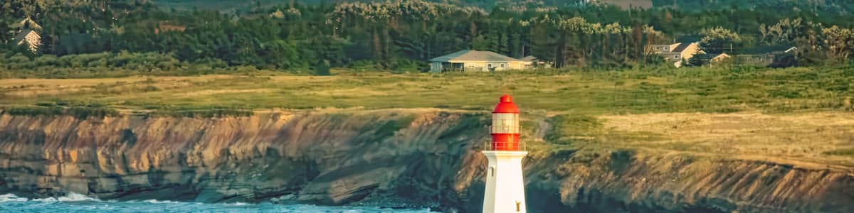 Un phare perché sur un promontoire rocheux, avec une ville côtière en arrière-plan.