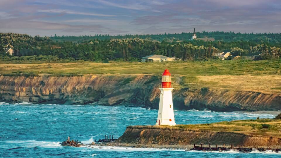 A lighthouse on a rocky outcrop with a coastal town in the background.