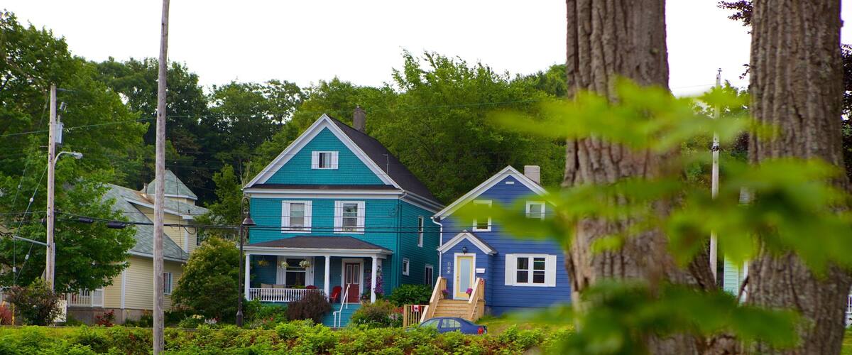 A row of two-story houses with a porch, surrounded by lush greenery and trees.