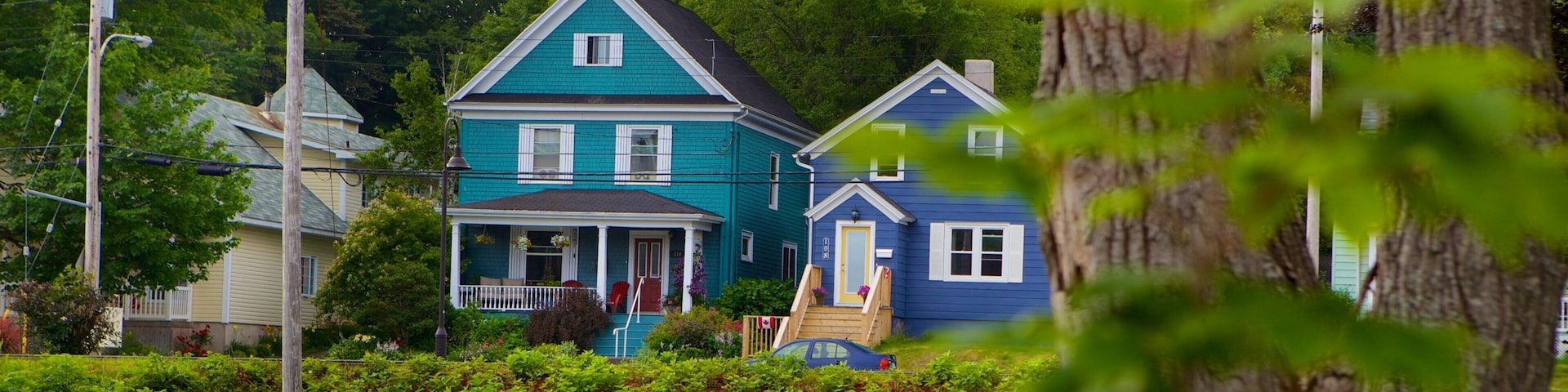 A row of two-story houses with a porch, surrounded by lush greenery and trees.