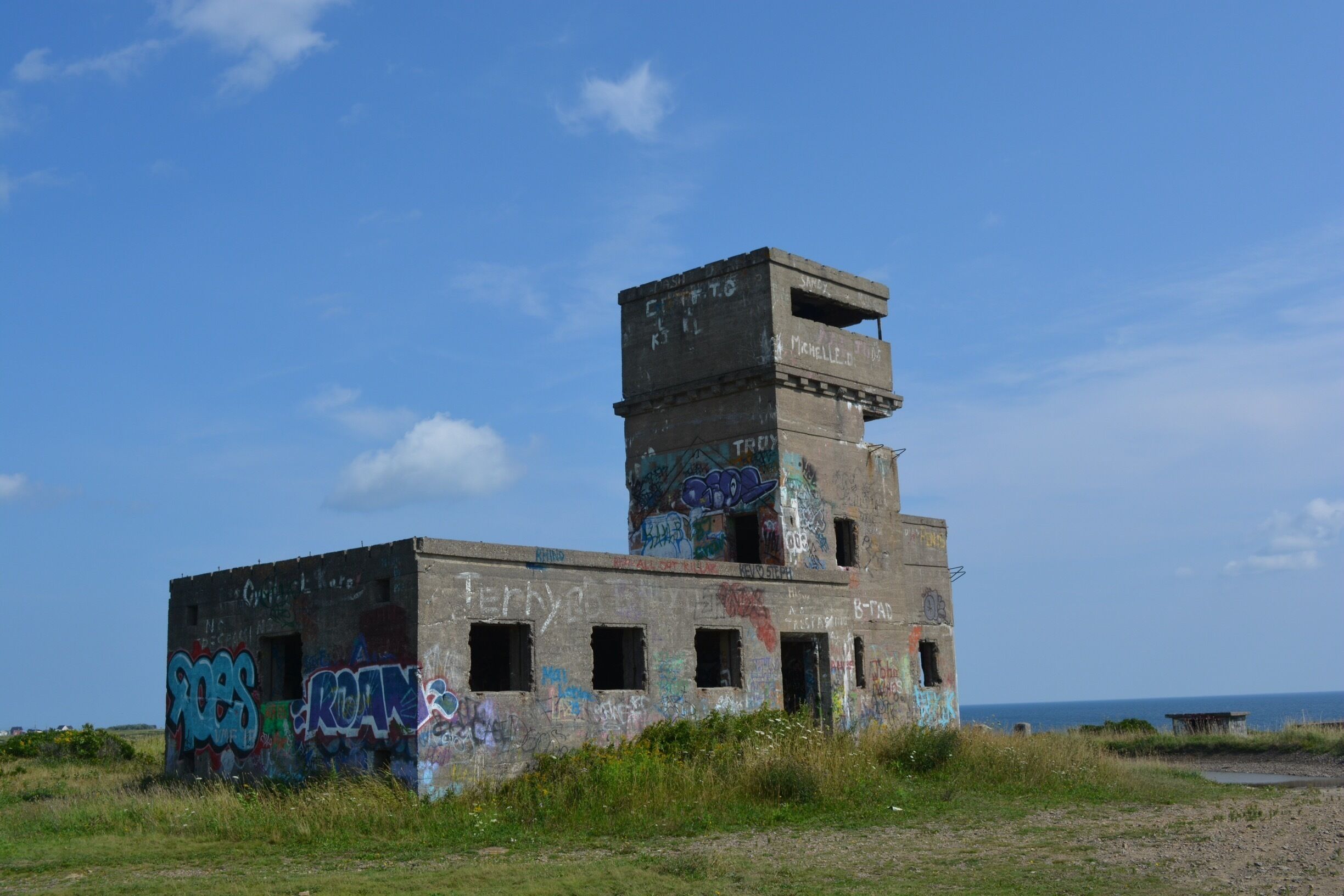 An abandoned building with graffiti and overgrown grass.