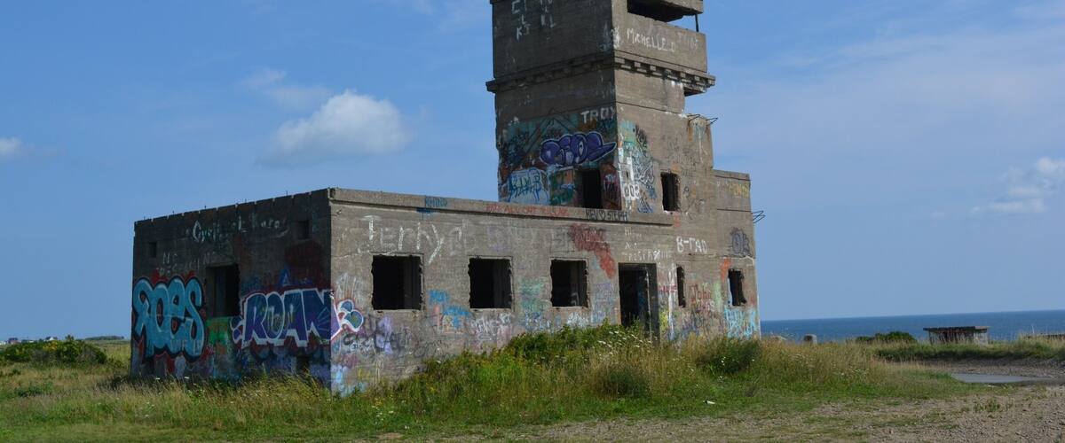 An abandoned building with graffiti and overgrown grass.