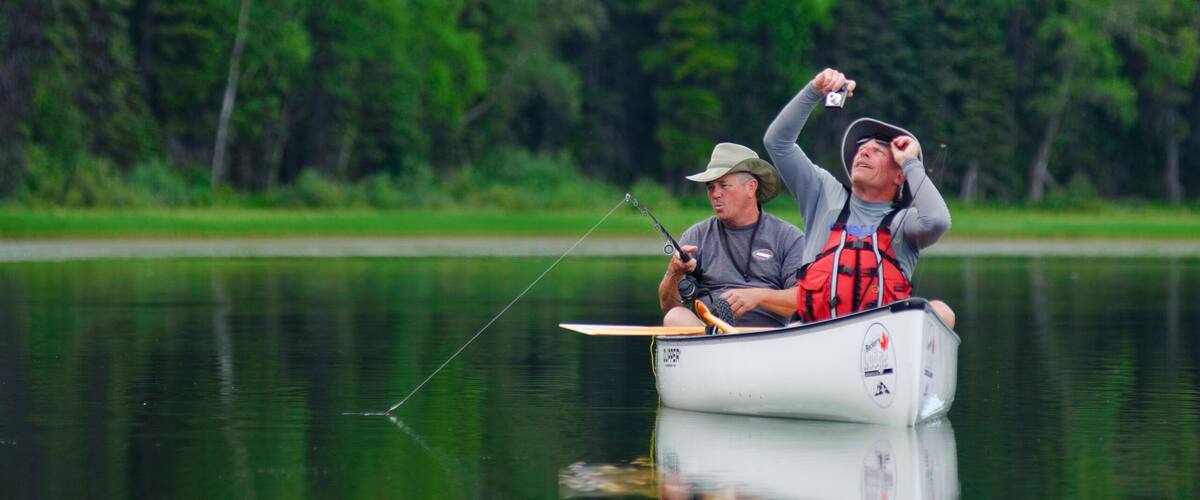 Two people in a small boat on a calm lake surrounded by dense forest.