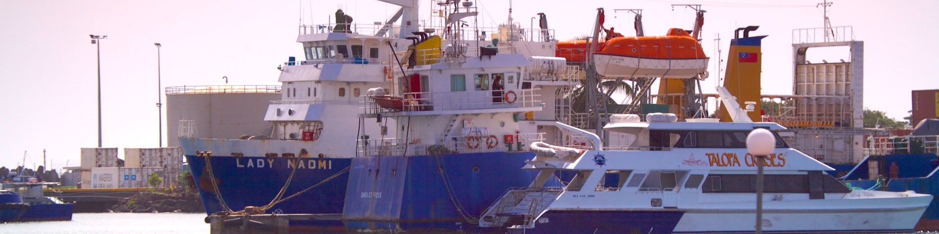 Un gran carguero llamado "Lady Naomi" atracado en un puerto, con embarcaciones más pequeñas cerca.