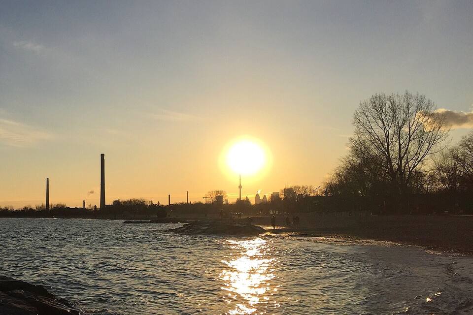 Een zonsondergang boven een wateroppervlak met industriële gebouwen op de achtergrond.