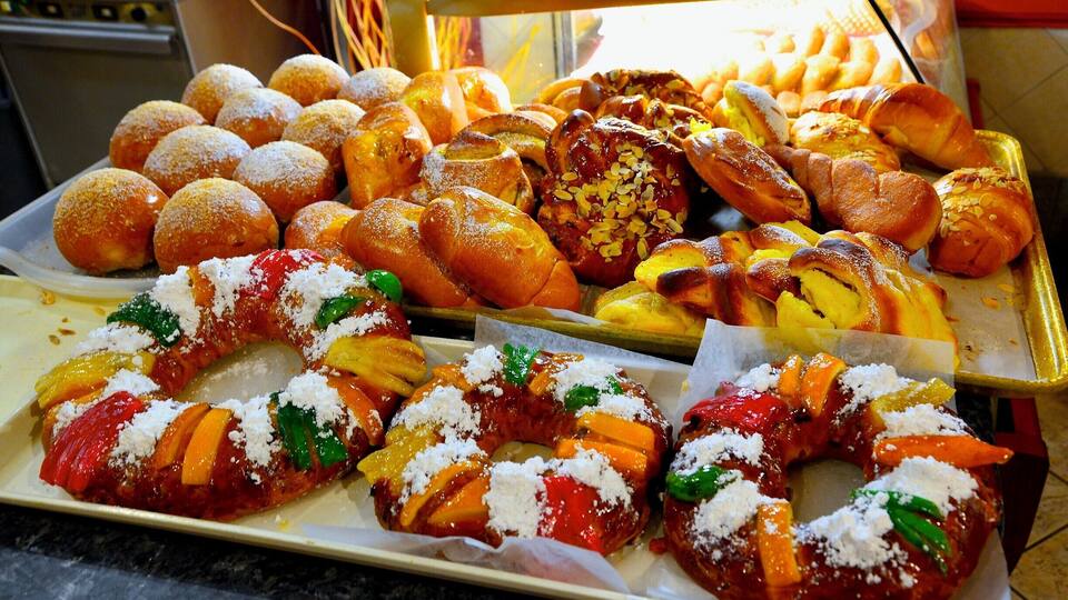 Diversos pastéis, incluindo sonhos, pães doces e um pastel com fruta e queijo.
