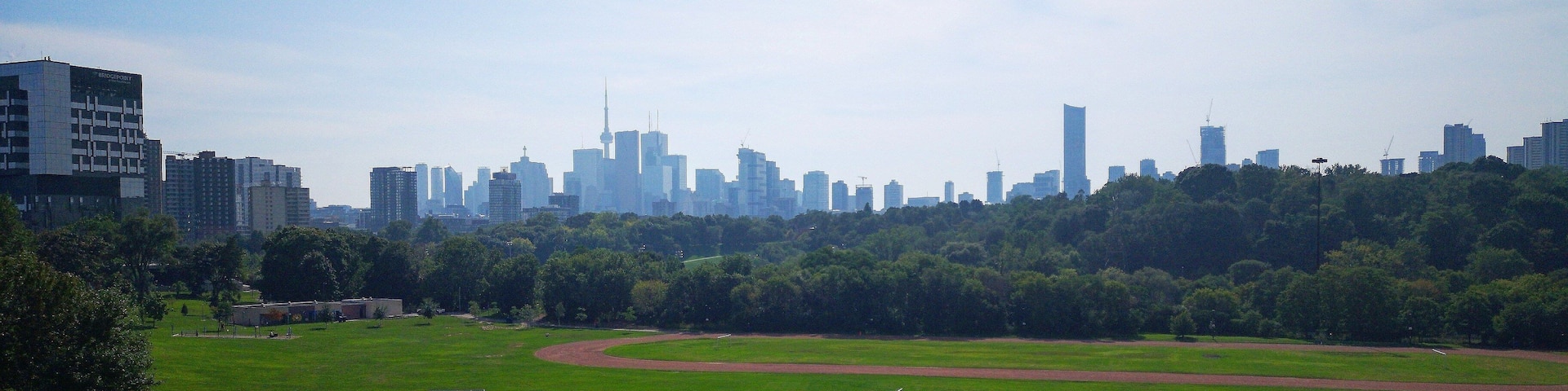 A park with a running track, a baseball diamond, and a city skyline in the background.
