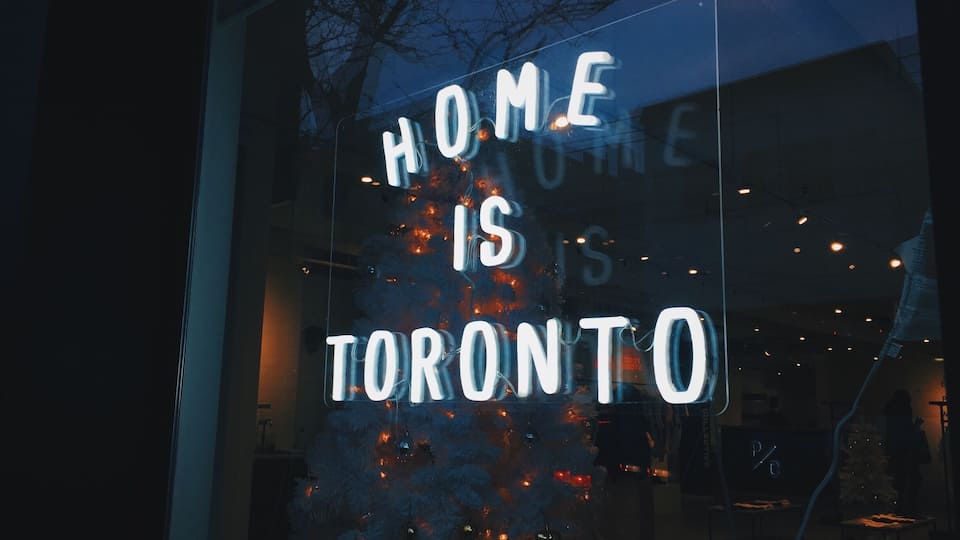 Árvore de Natal com luzes e um letreiro neon que diz 'HOME IS TORONTO'.