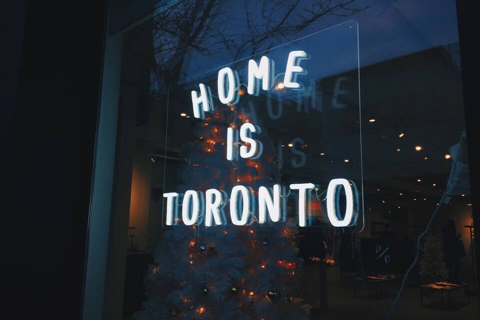 A Christmas tree with lights and a neon sign that reads "HOME IS TORONTO".