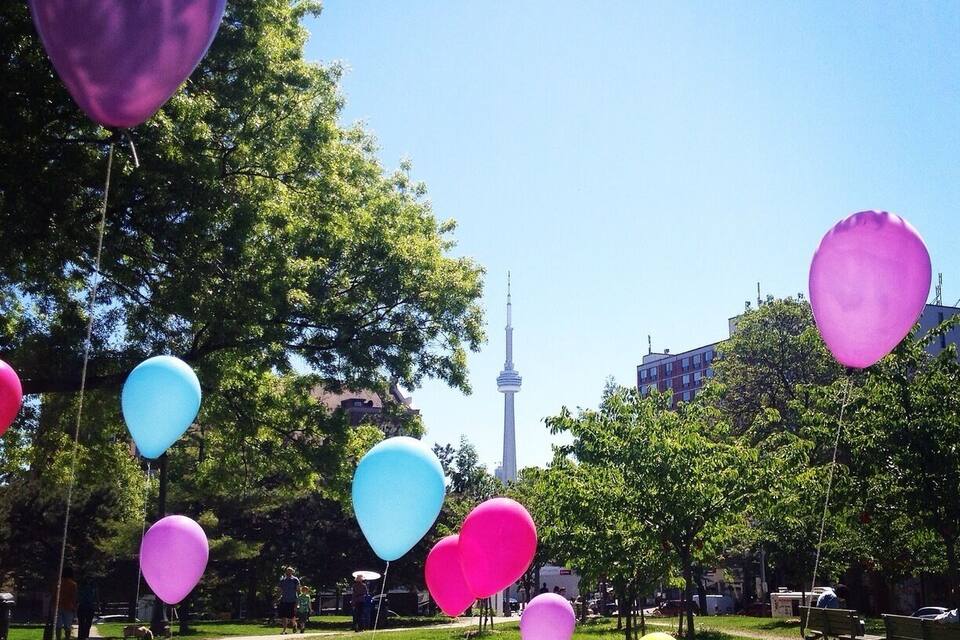 A park with colorful balloons, green grass, trees, and a tower in the background.