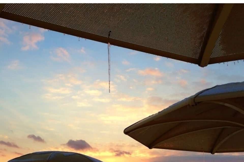 A beach with umbrellas and a sunset over the water.