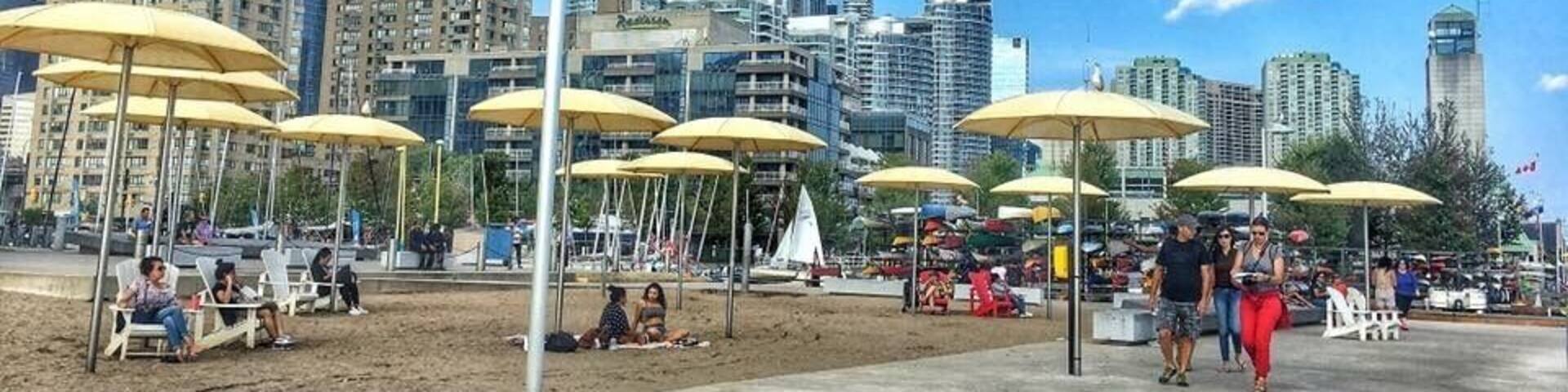 A beach with yellow umbrellas, people, and a cityscape with tall buildings in the background.