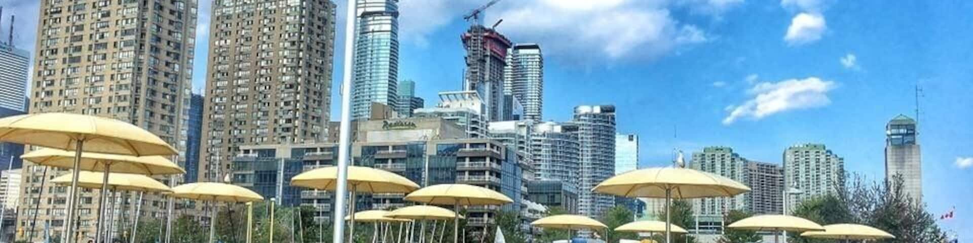 Una playa con sombrillas amarillas, gente y un paisaje urbano con edificios altos al fondo.