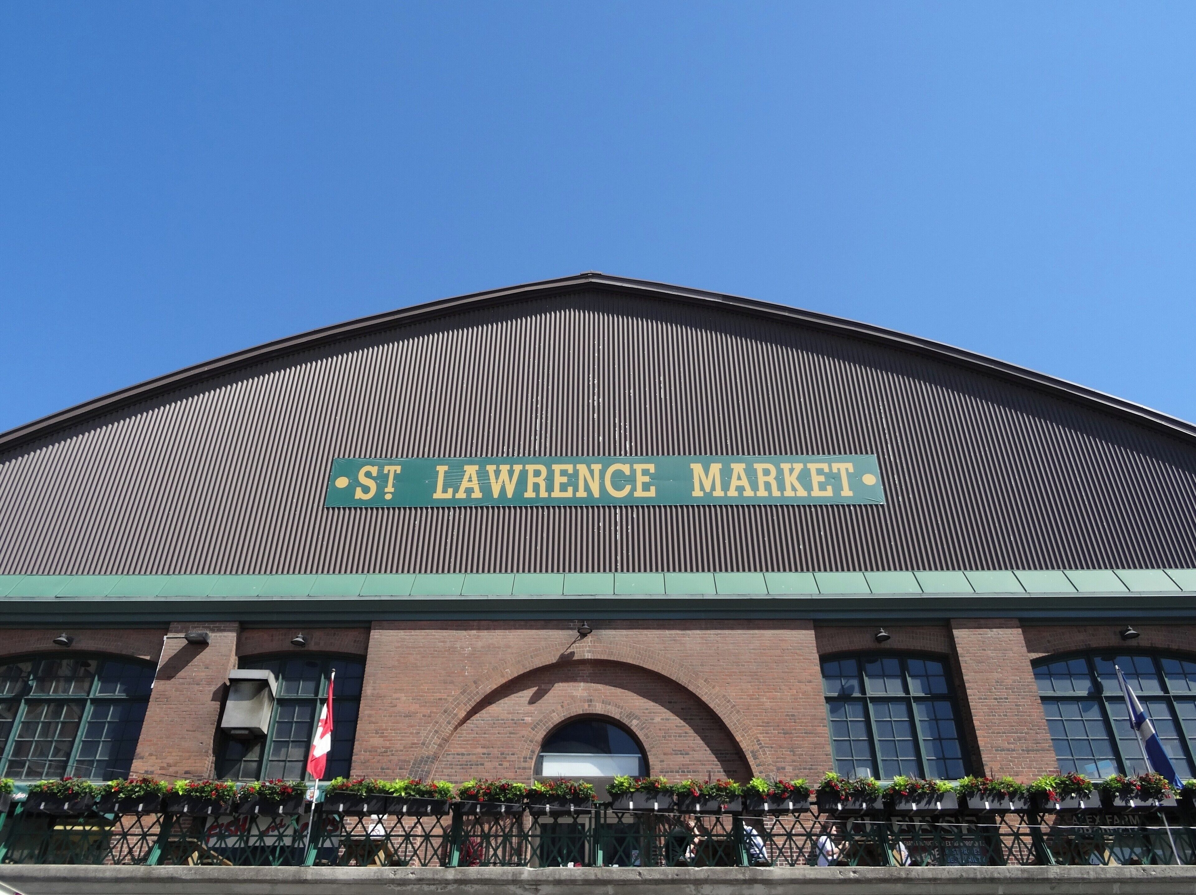 The exterior of St. Lawrence Market with a green sign, brick facade, and arched windows.