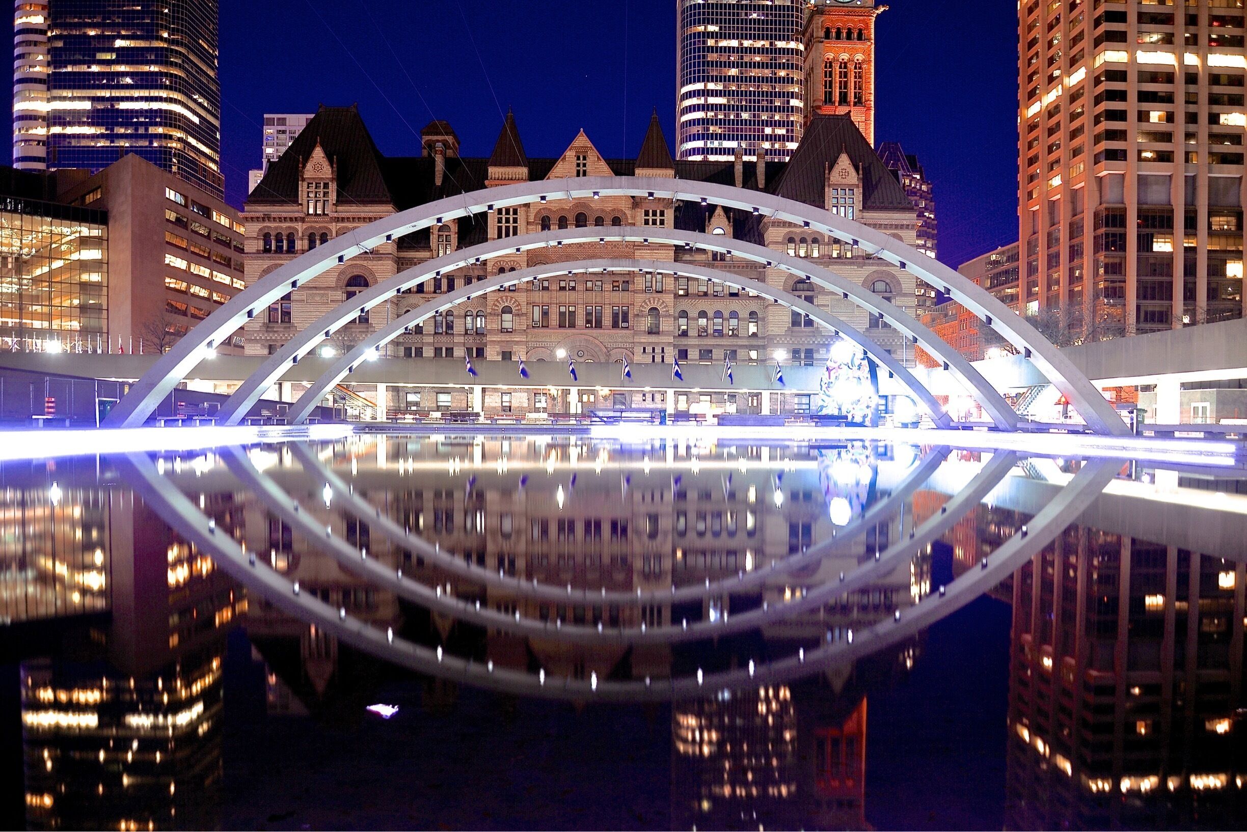 A modern bridge with a reflection in the water, surrounded by historic buildings and tall skyscrapers.