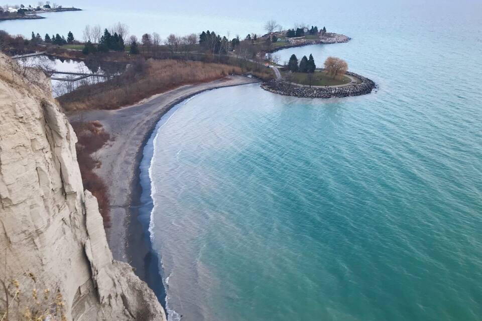 Eine Küstenlandschaft mit einer Klippe, einem Sandstrand und ruhiger See.
