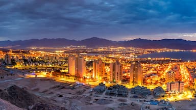 Un paisaje urbano al atardecer con edificios iluminados y montañas al fondo.