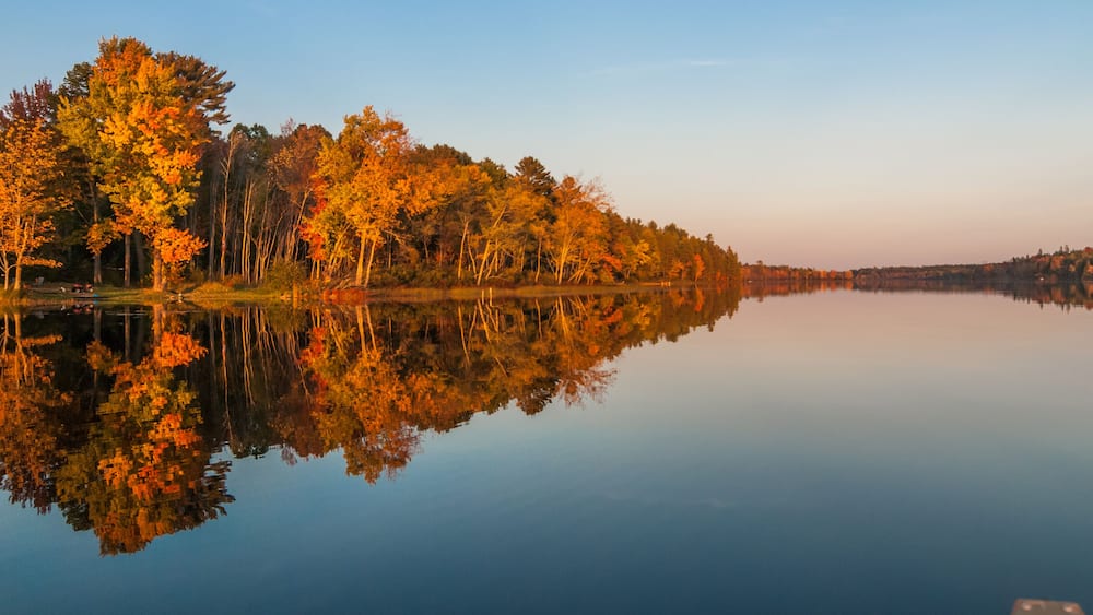 A calm lake reflecting autumn trees.