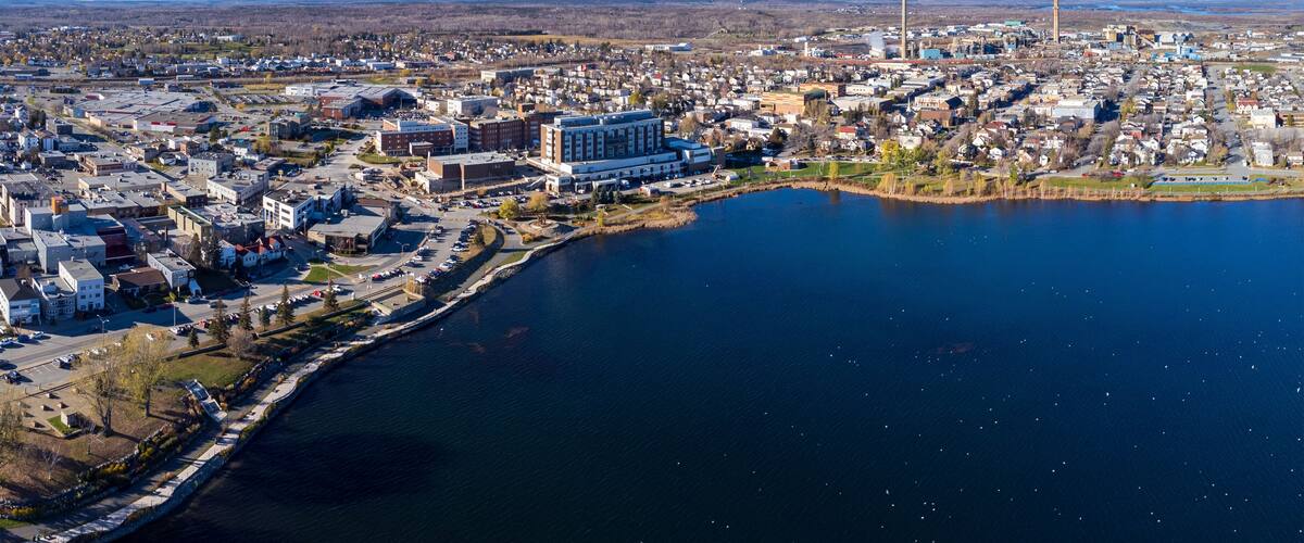 A lakeside town with industrial buildings, a large water body, and distant hills.
