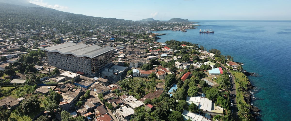 An aerial view of a coastal town with a large industrial building, dense housing, and a harbor with ships.