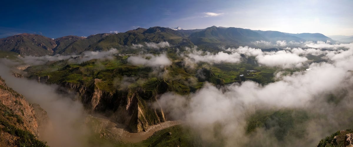 A mountainous landscape with a valley shrouded in clouds, terraced fields, and a river.
