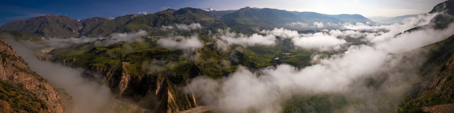 A mountainous landscape with a valley shrouded in clouds, terraced fields, and a river.