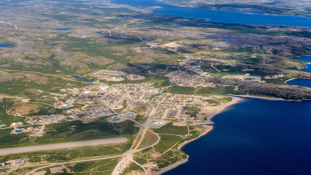 Vue aérienne d’une ville côtière avec un ensemble dense de bâtiments, une route principale et une zone de plage.