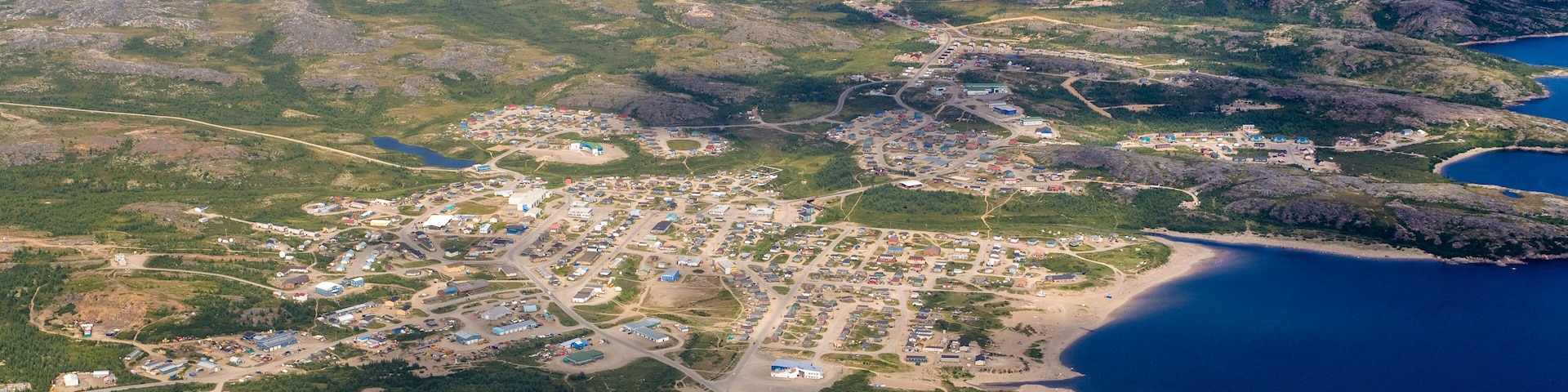 Vista aérea de un pueblo costero con un conjunto denso de edificios, una carretera principal y una zona de playa.