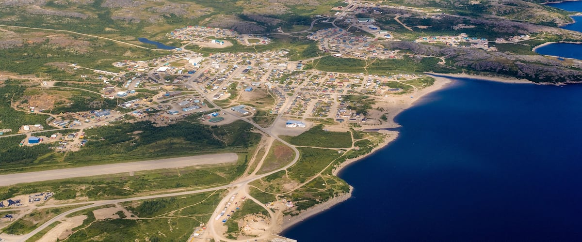 An aerial view of a coastal town with a dense cluster of buildings, a main road, and a beach area.