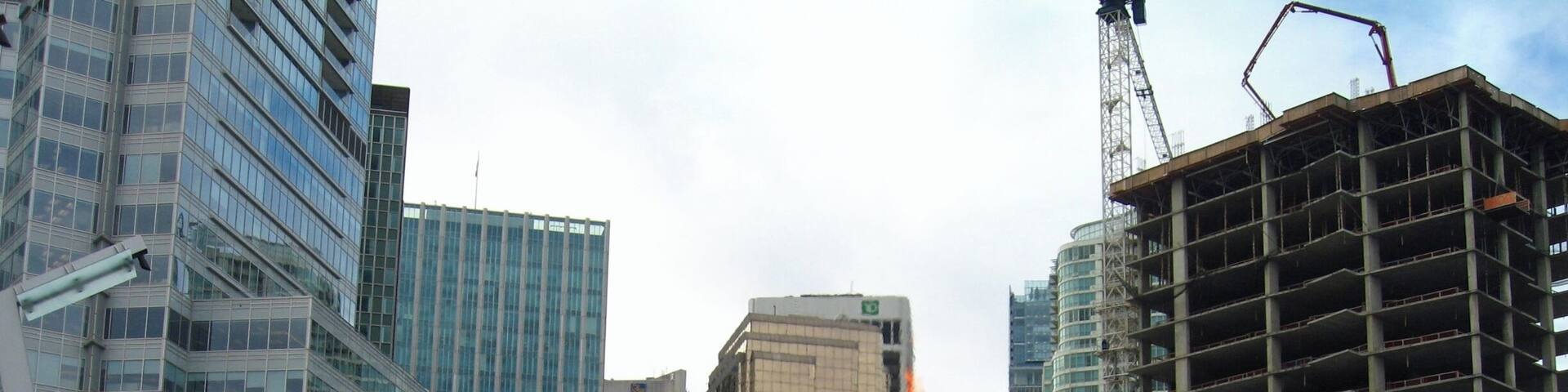 A cityscape with modern buildings, a large metal sculpture, and a construction site.