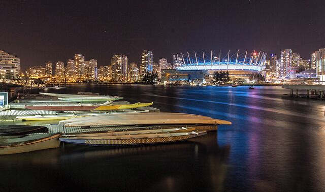 A waterfront with boats docked, a city skyline, and a stadium with lights.