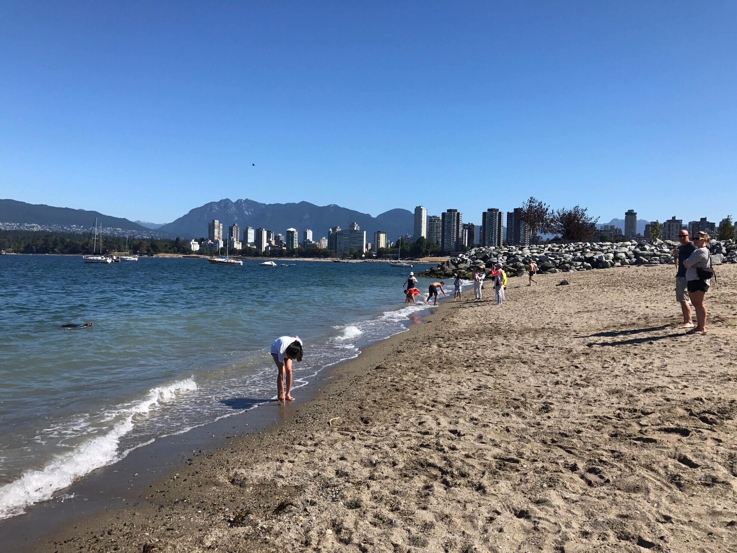 Una playa con gente, un horizonte urbano y montañas al fondo.