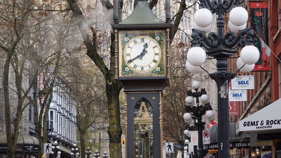 Uma rua com uma torre do relógio, uma estátua e um edifício com a placa 'GEMS & ROCKS'.