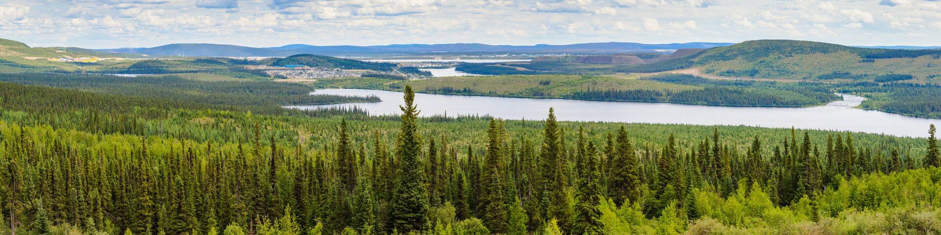 A mountainous landscape with dense forests, a lake, and a distant town.