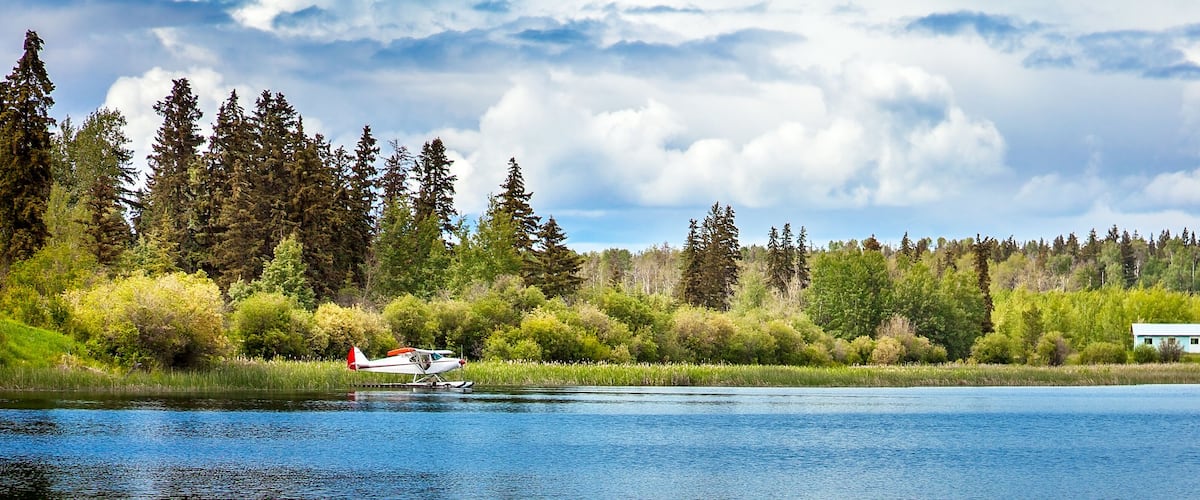 A seaplane on a lake with a forest and a house in the background.