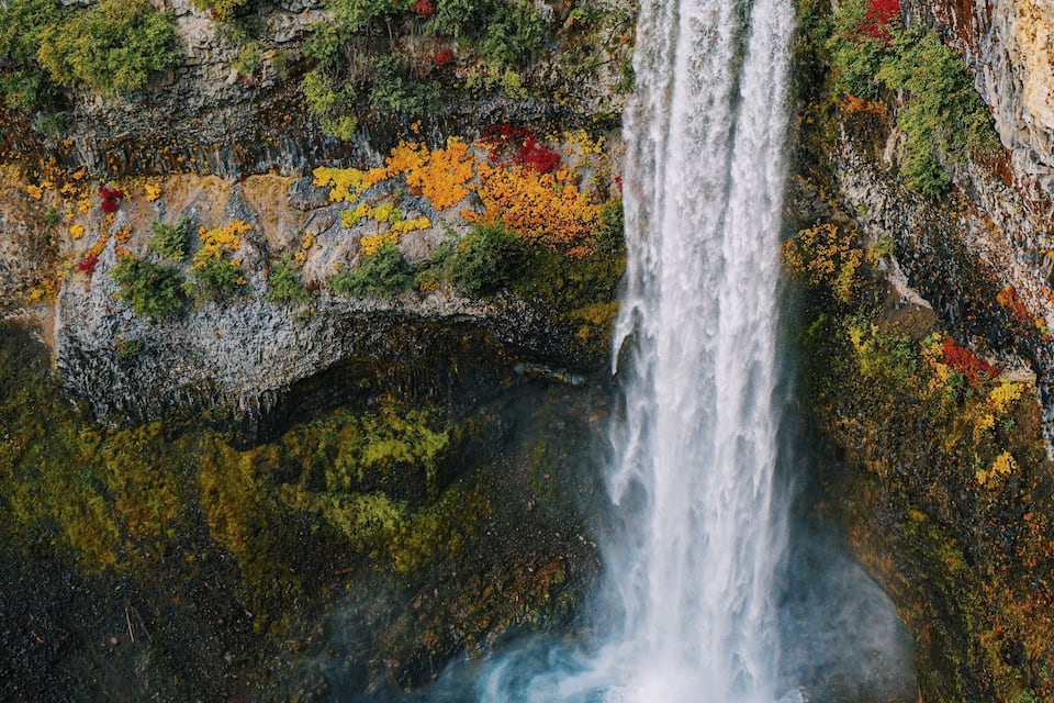 A waterfall cascading into a pool surrounded by rocky cliffs and autumn-colored foliage.