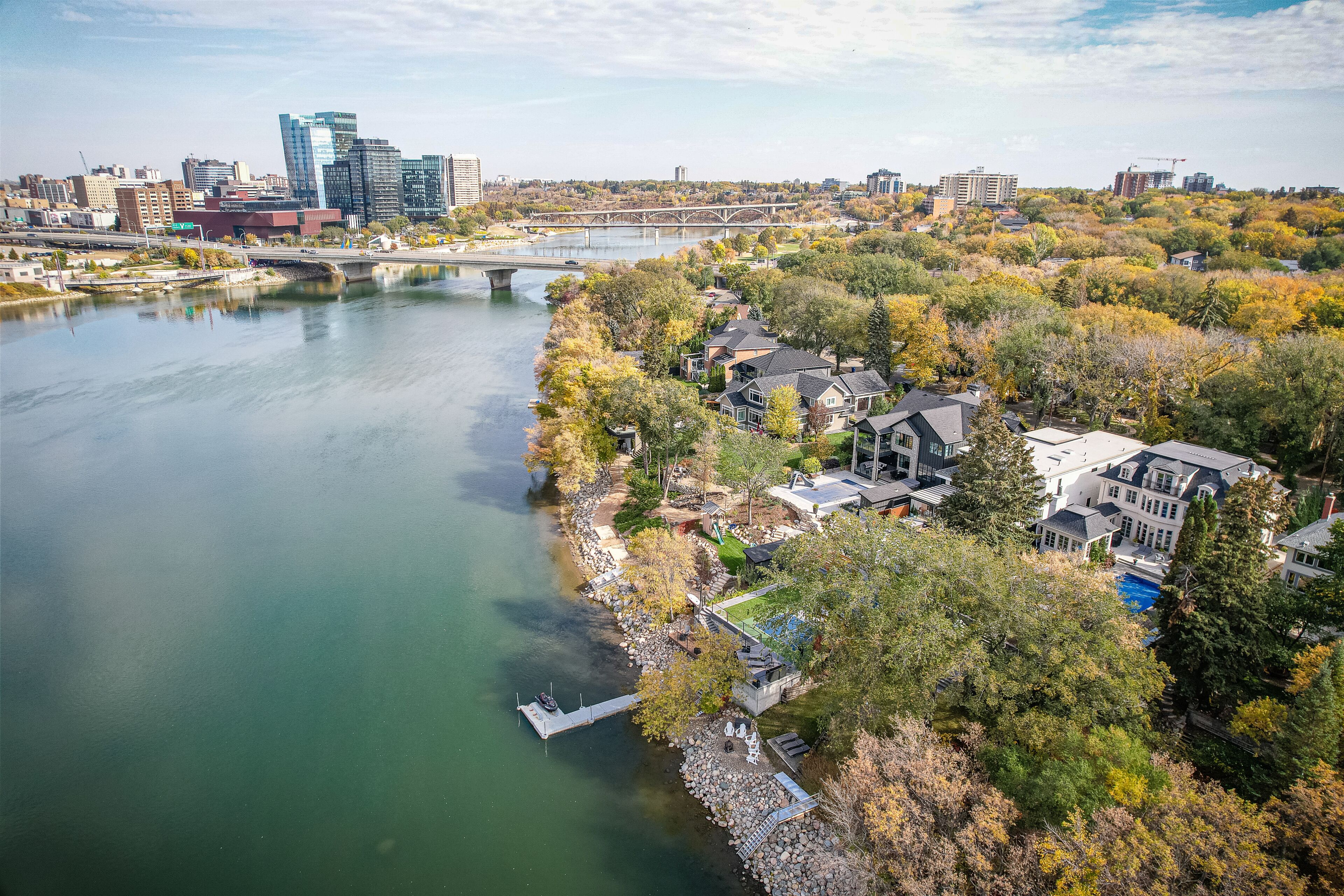 A river with a bridge, a residential area with houses, and a city skyline in the background.