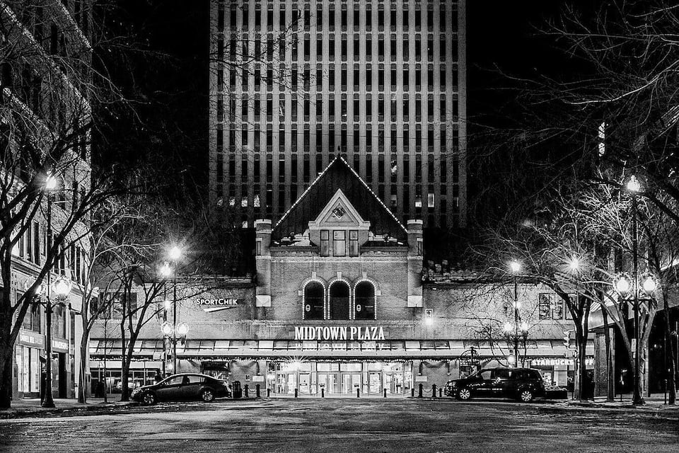 A nighttime view of Midtown Plaza with illuminated storefronts and a prominent building with arched windows.
