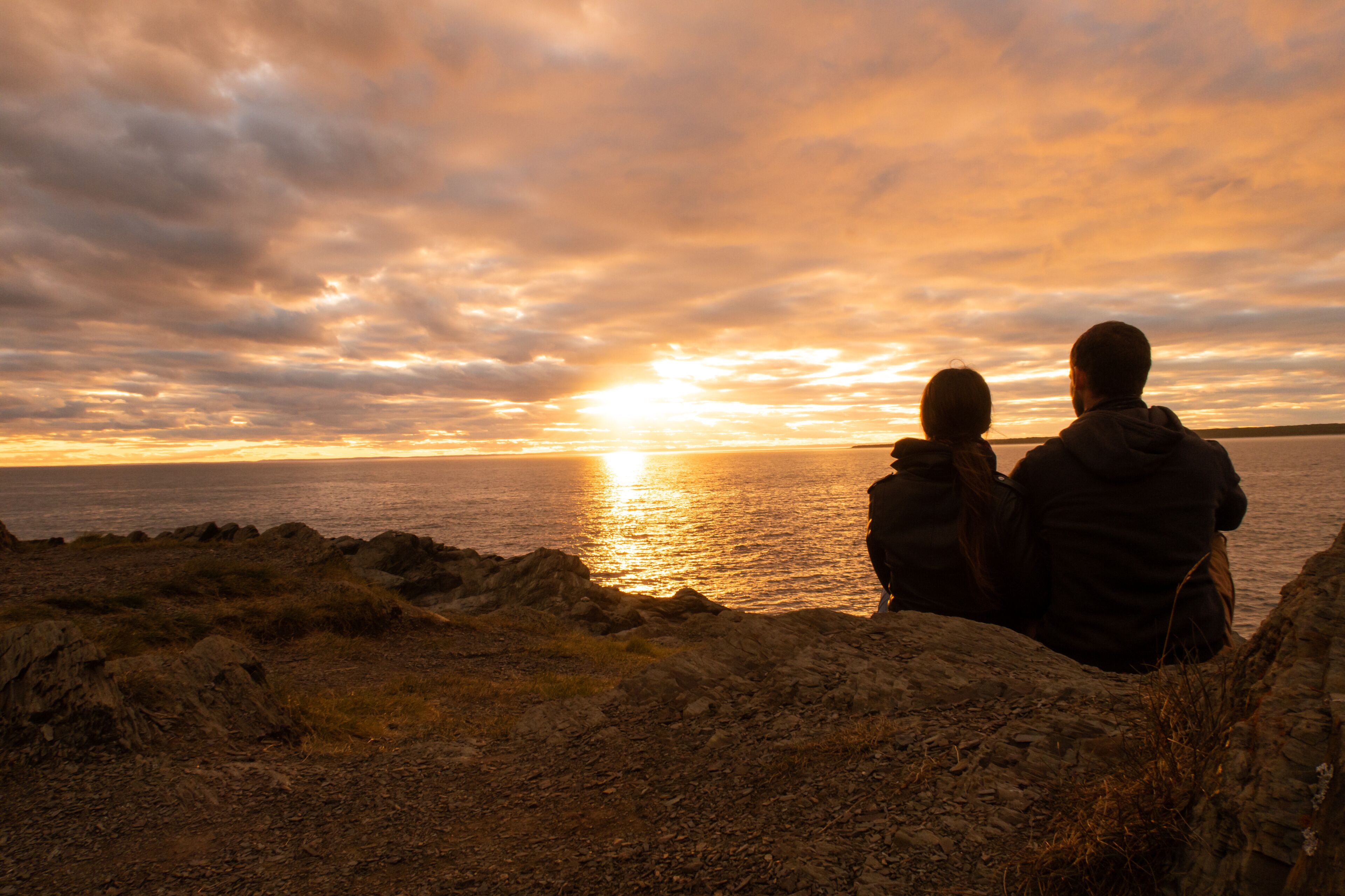 Young couple sitting on a cliff and admiring the sunset in the Bic national park, Canada