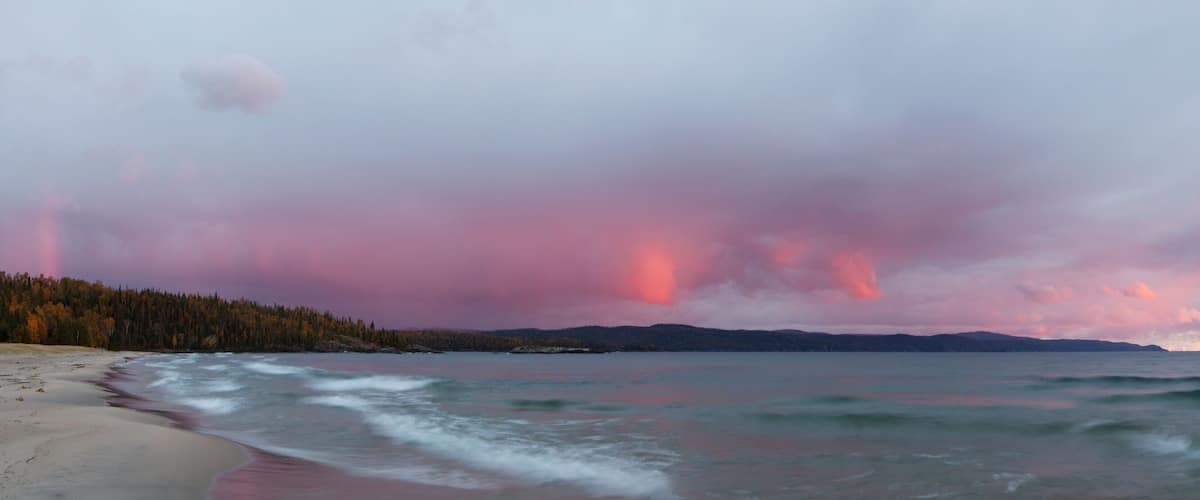 A beach with waves, a forest, and mountains in the distance.