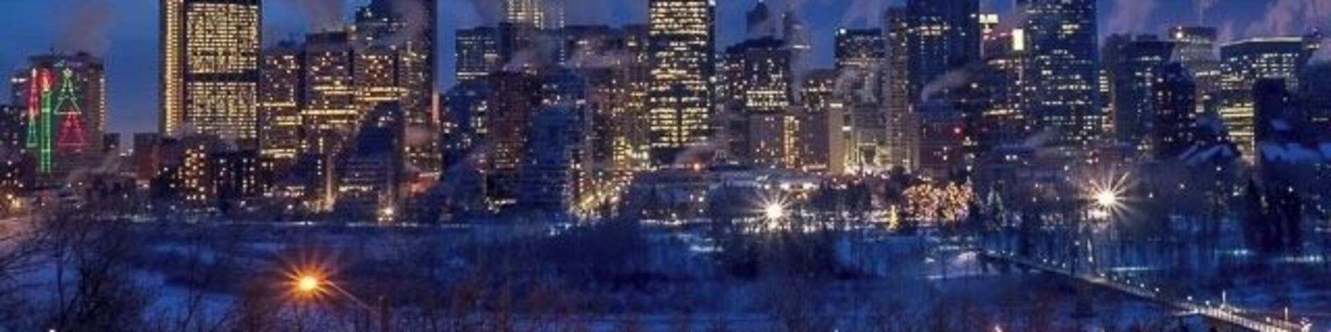 Un horizonte urbano al atardecer con edificios iluminados y un paisaje cubierto de nieve.