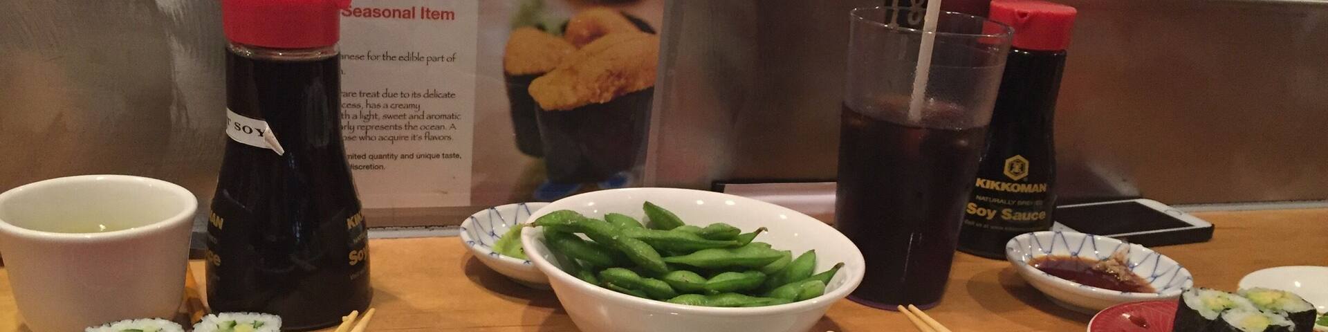 A sushi bar with various types of sushi, soy sauce, and green beans.