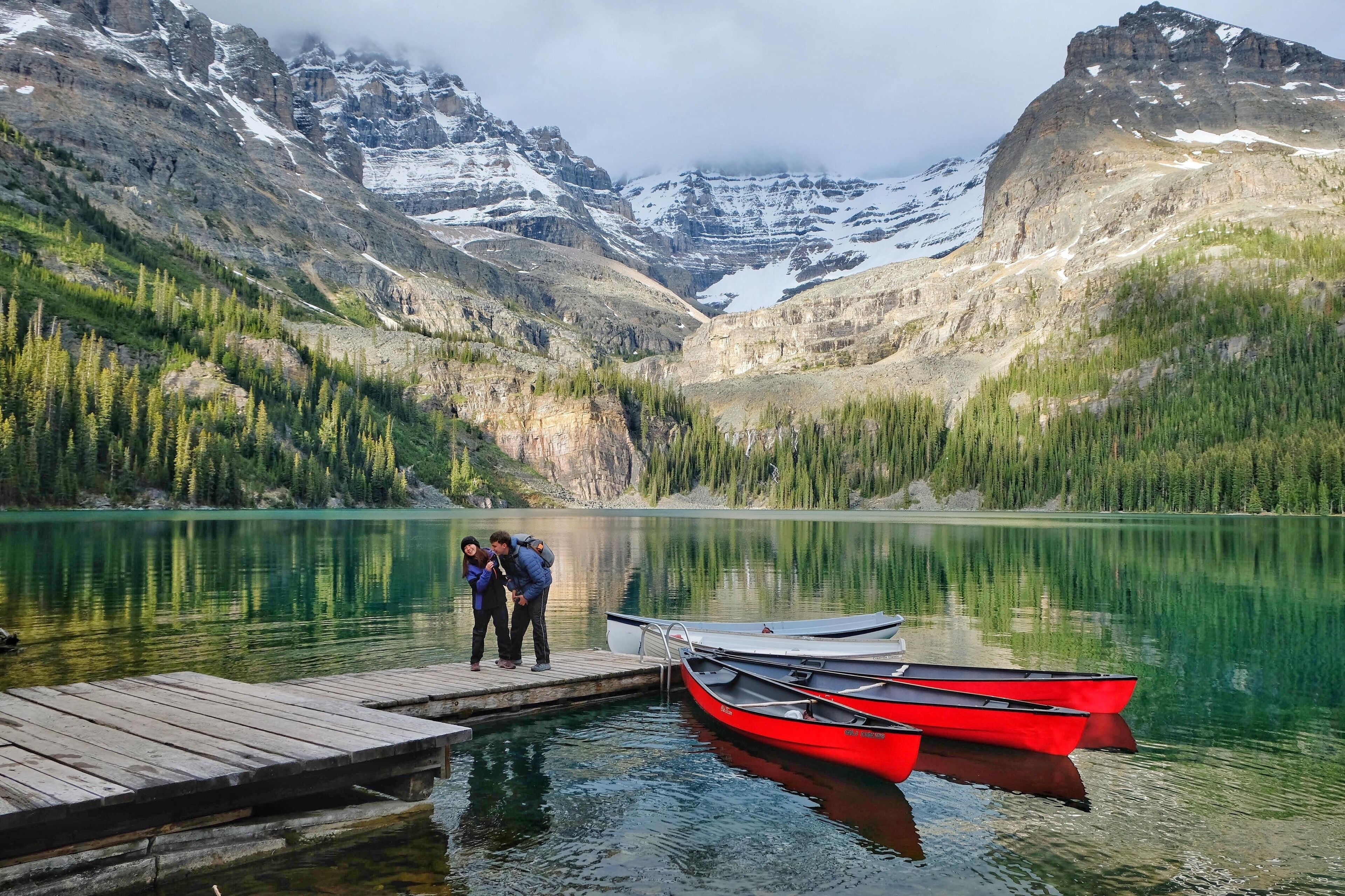 A calm lake surrounded by mountains with a wooden dock and red boats.