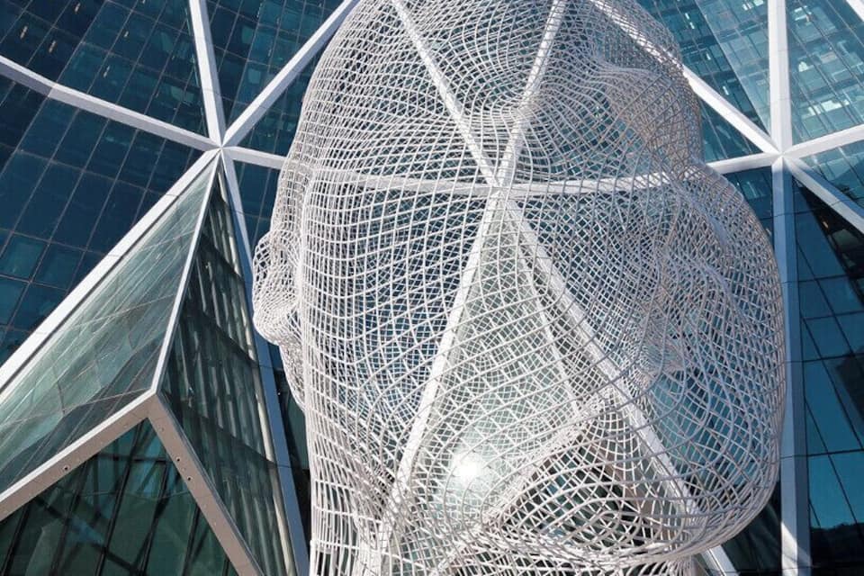 Un edifici modern de vidre amb una escultura esfèrica de metall al davant.