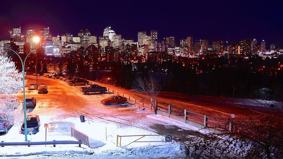 A snowy parking lot with cars and a city skyline in the background.